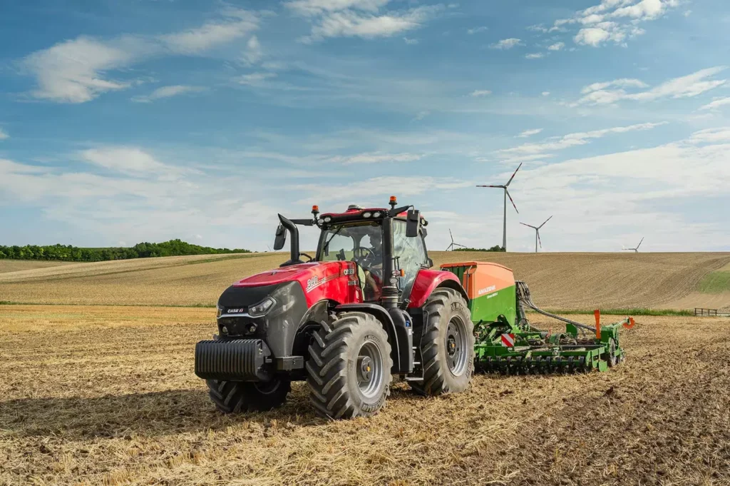 Case IH Magnum 380-traktor koblet til en Amazone såmaskin, arbeider på et jorde med vindturbiner i bakgrunnen.