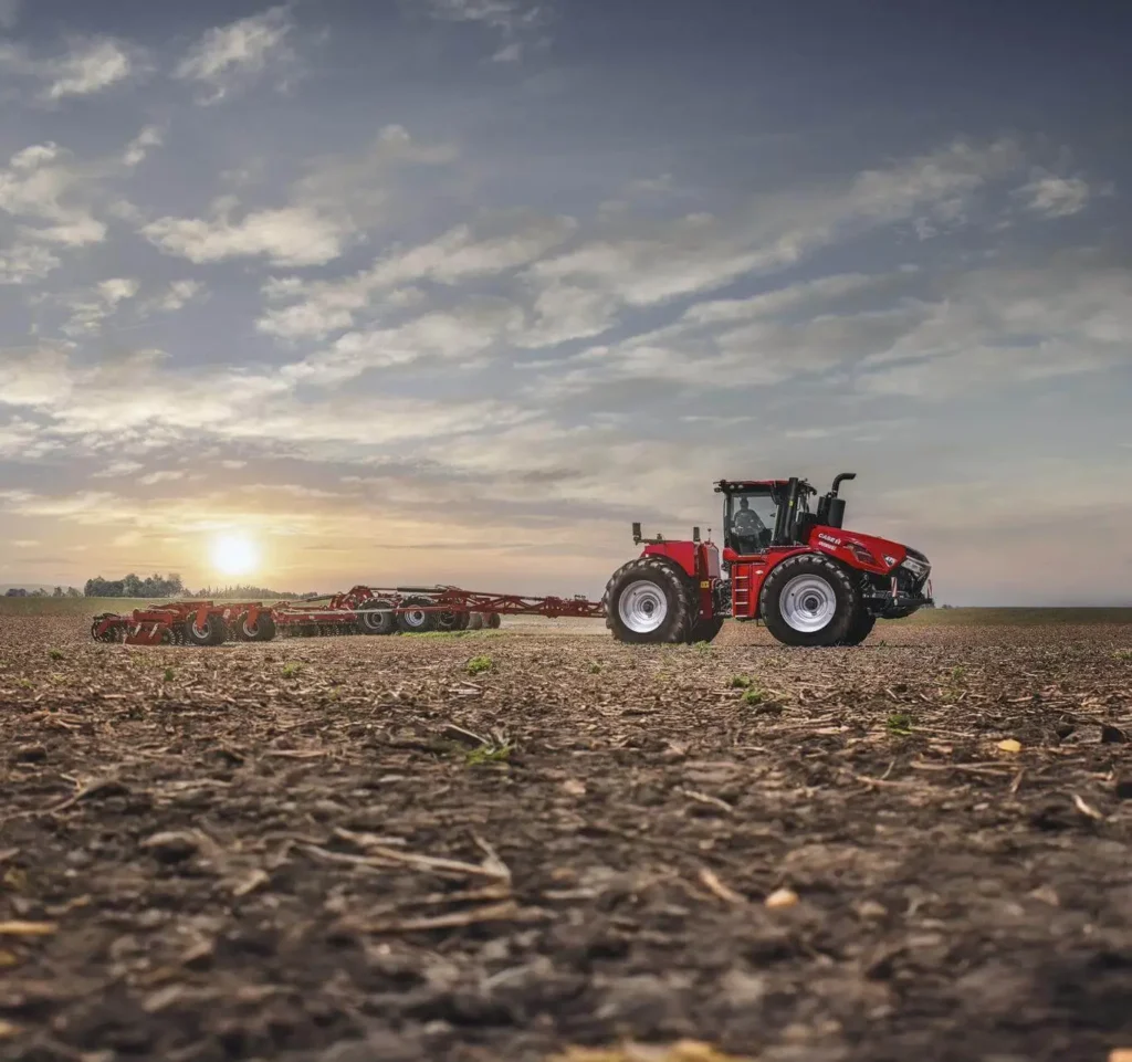 8. Case IH traktor jobber på en åker med en stor skålharv bak, soloppgang i bakgrunnen.