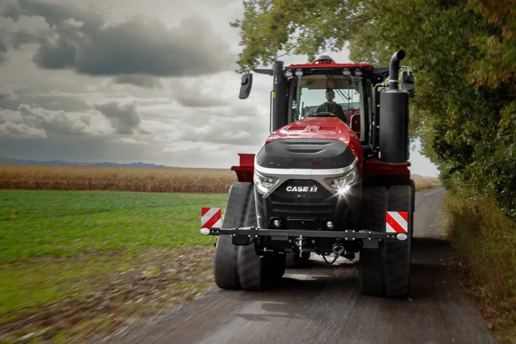 Case IH Quadtrac traktor kjører på en smal vei omgitt av åkre og trær.