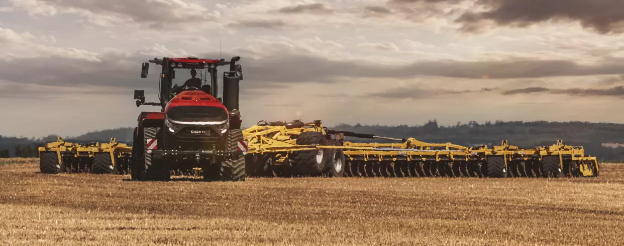 Frontbilde av Case IH Quadtrac 715 AFS Connect™ – Kraftig traktor med beltedrift, sett forfra i åkeren ved soloppgang.