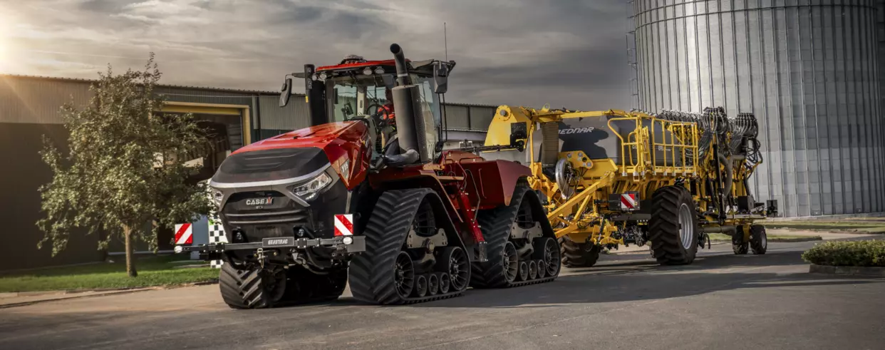 Quadtrac 715 AFS Connect™ foran industribygninger – Kraftig traktor med beltedrift koblet til en gul maskin.