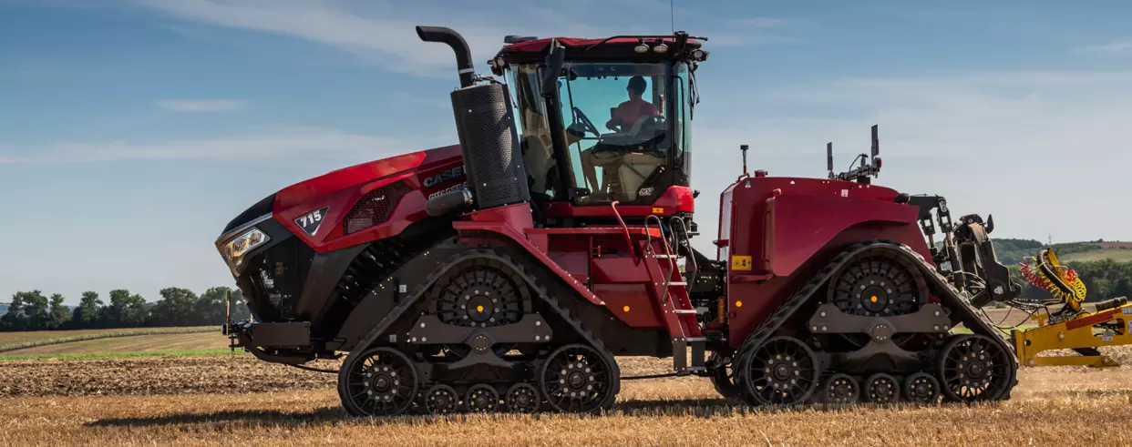 Sidevisning av Case IH Quadtrac 715 AFS Connect™ i felt – Traktoren med beltedrift arbeider på en åker under blå himmel.