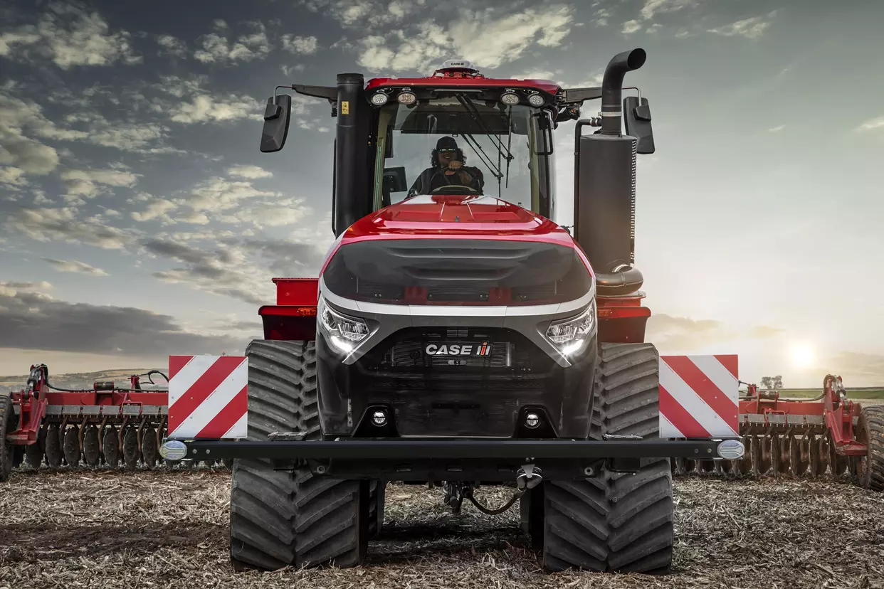 Sidevisning av Case IH Quadtrac 715 AFS Connect™ i felt – Traktoren med beltedrift arbeider på en åker under blå himmel.