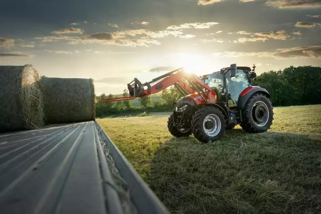 Case IH Vestrum traktor med frontlaster som løfter rundballer i solnedgang.