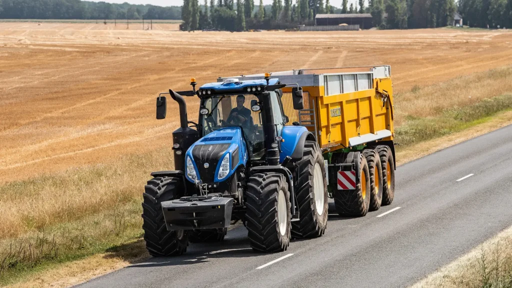 New Holland T8 Genesis kjører på vei med gul kornhenger