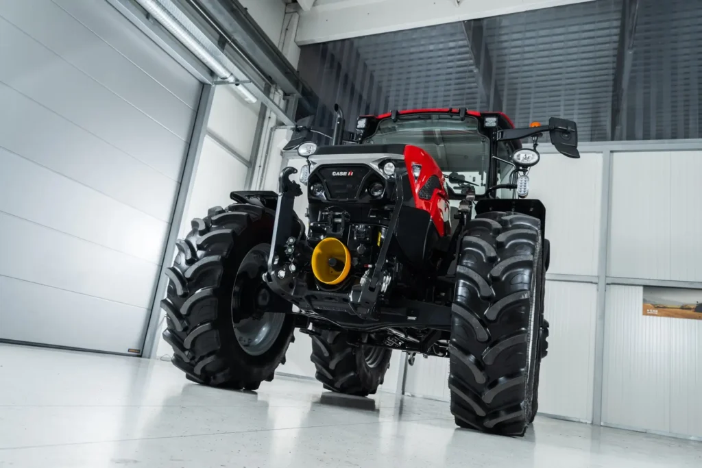 En Case IH Farmall 120C-traktor sett forfra i en innendørs hall med lys grå vegger og tak. Traktoren har store, robuste hjul og en kraftig front.