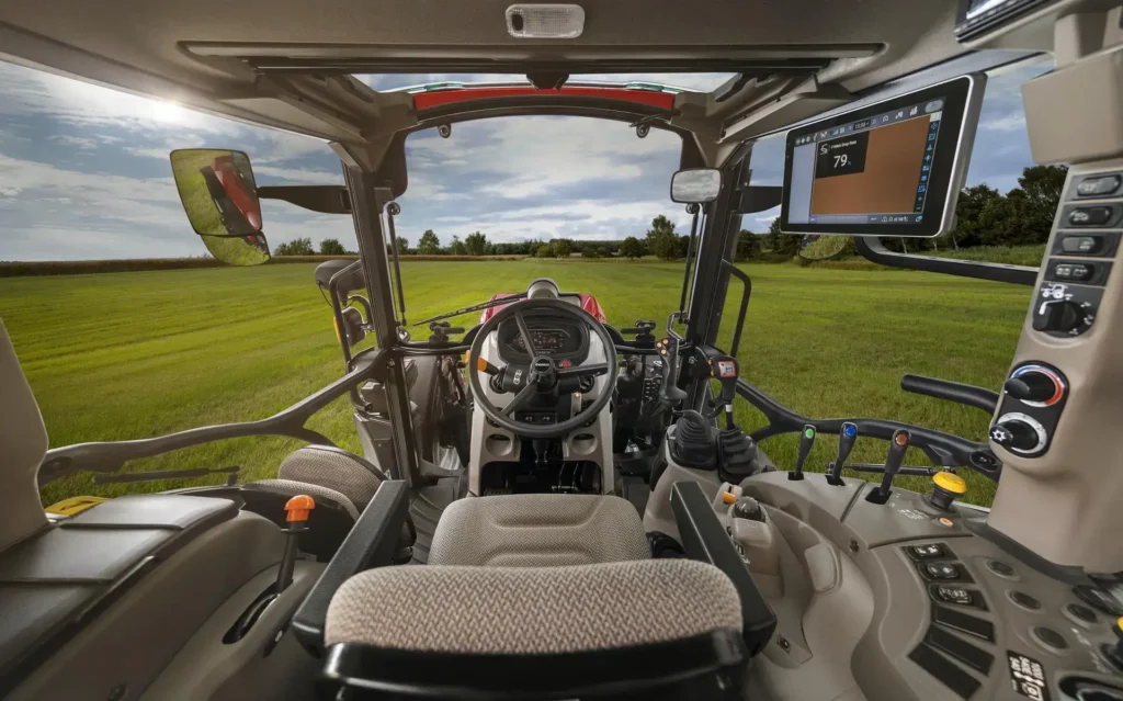 Innvendig førerhus på en Case IH Farmall 120C-traktor, med et moderne kontrollpanel, skjerm og spaker, samt en utsikt over en grønn eng.