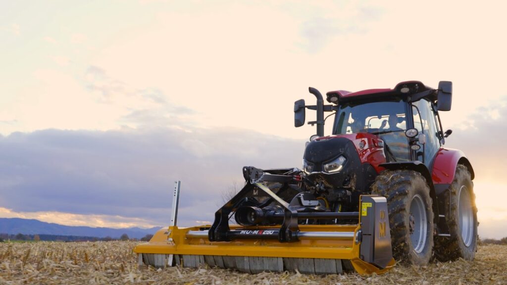 Case IH Maxxum traktor med en gul beitepusser, arbeider på et jorde ved solnedgang.