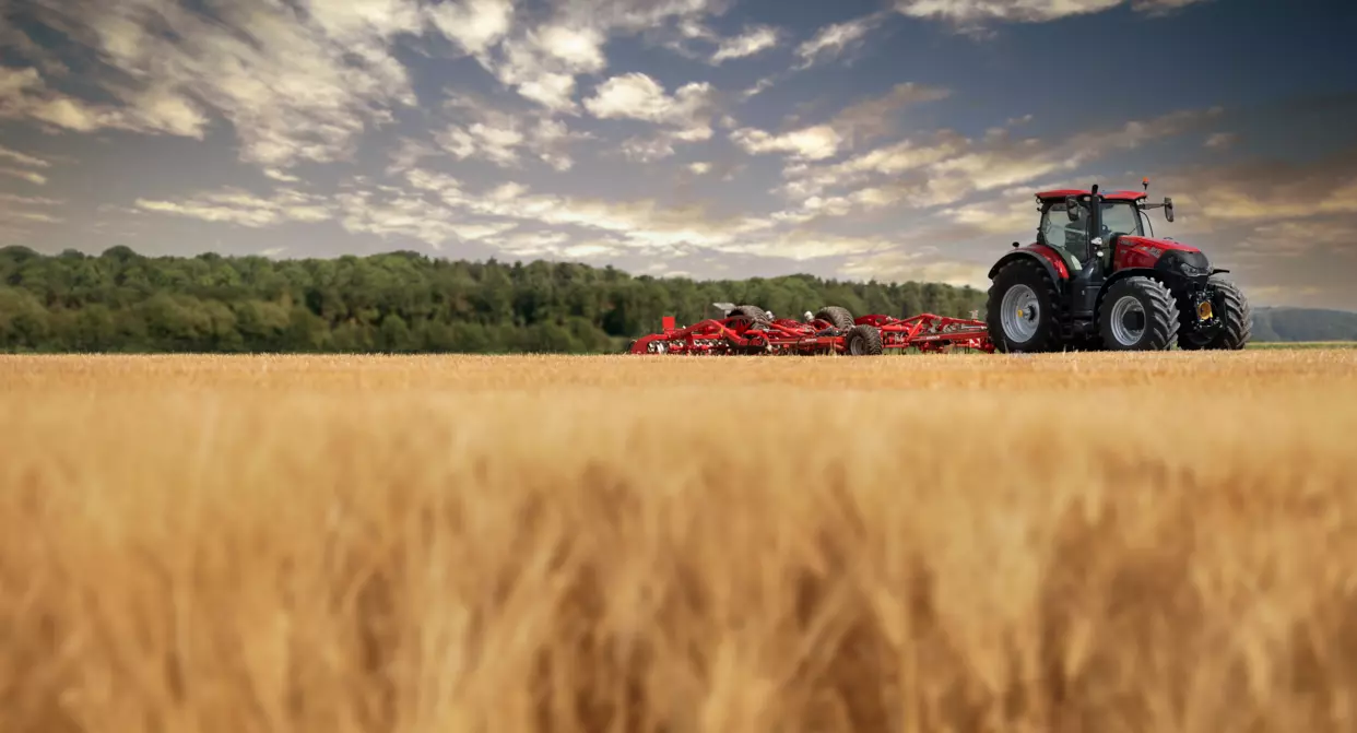 Case IH Optum-traktor arbeider på et jorde ved solnedgang med en stor jordbruksredskap festet bak.