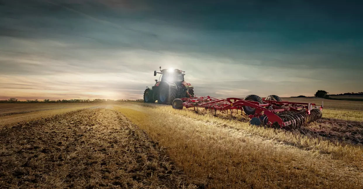 Case IH Optum 340 AFS Connect traktor kjører på en landevei med henger, med blå himmel og åkre i bakgrunnen.