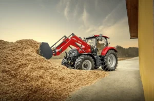 En rød Case IH-traktor med frontlaster som arbeider ved en stor haug med flis nær en gul