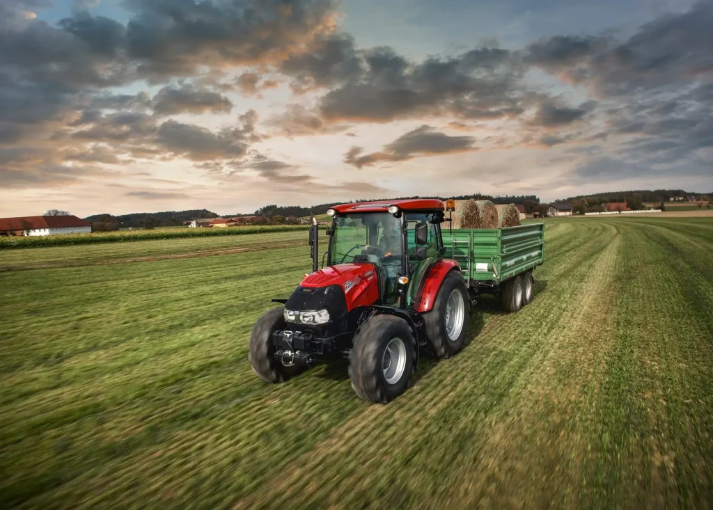 Case IH 75A traktor som trekker en tilhenger med høyballer på en åker ved solnedgang