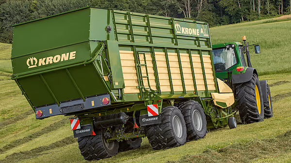 Traktor med påmontert grønn KRONE AX silotransportvogn med åpen tippemekanisme i drift.