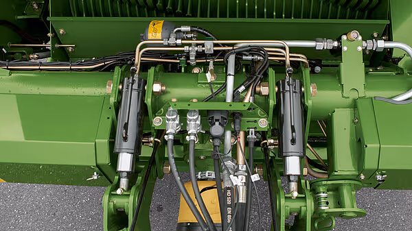 Hydraulisk system og komponenter under hengeren med rørsystem, ventiler og monteringsdetaljer på grønn bakgrunn.