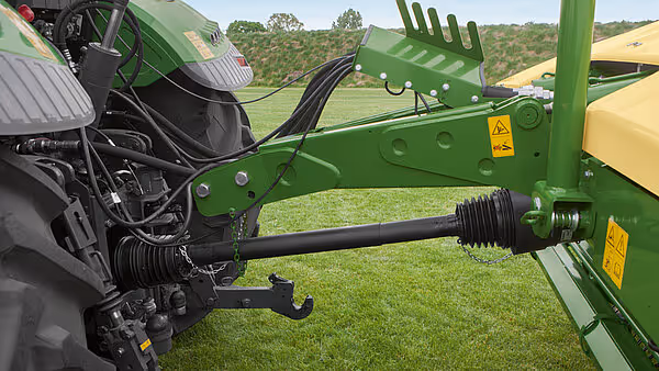 Kartoffelskuff med kardanaksel montert på grønt Krone-tilbehør, vist fra siden med landbrukslandskap i bakgrunnen.