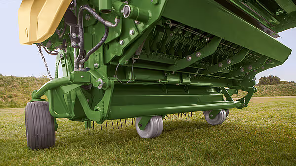 Sidevisning av KRONE AX høstmaskin med grønt rammeverk, gul høstekurv og hydrauliske sylindre montert på grønt understell med store hjul på grasslått mark.