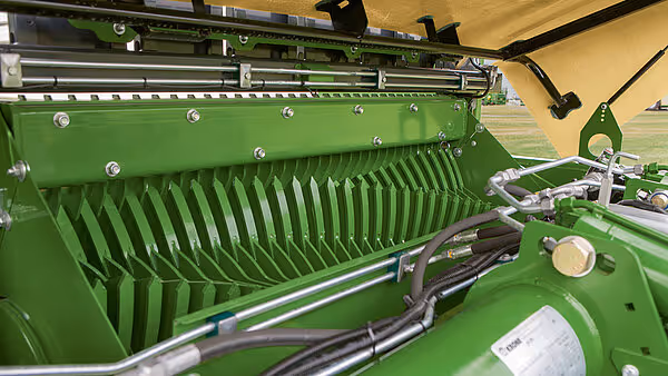 Nærbilde av høstemekanismen på KRONE AX med vertikale tinder for oppsamling av høy og hydrauliske ledninger montert på grønt rammeverk.