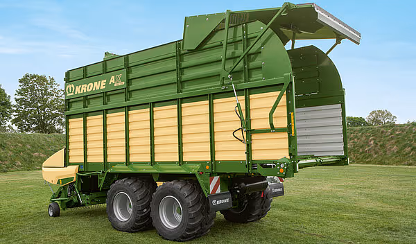 KRONE AX-vogn i grønt og gult med åpne sidelister og presseekspander montert på traktor.