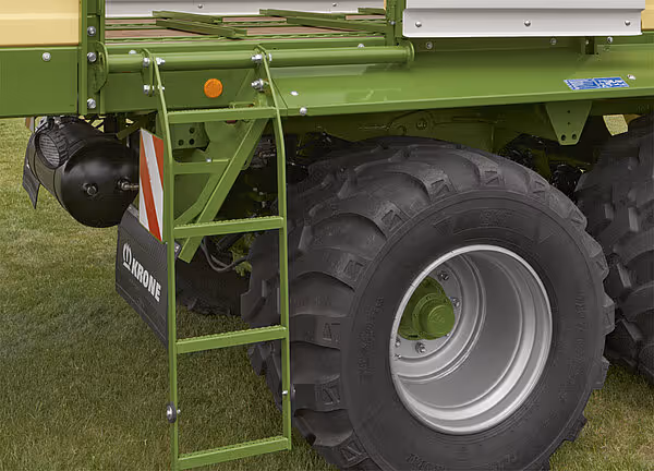 Nærbilde av høyre side av KRONE AX vogn med grønt chassis, sorte landbruksdekk på aluminum felg, og grønn stige for innstigning.