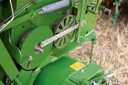 Detaljbilde av drivverk og mekaniske komponenter på en KRONE rundballpresse, med synlig fjær og drivhjul.