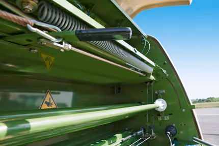 Hydrauliske slanger og komponenter på undersiden av en KRONE rundballpresse, med advarselsmerking synlig.