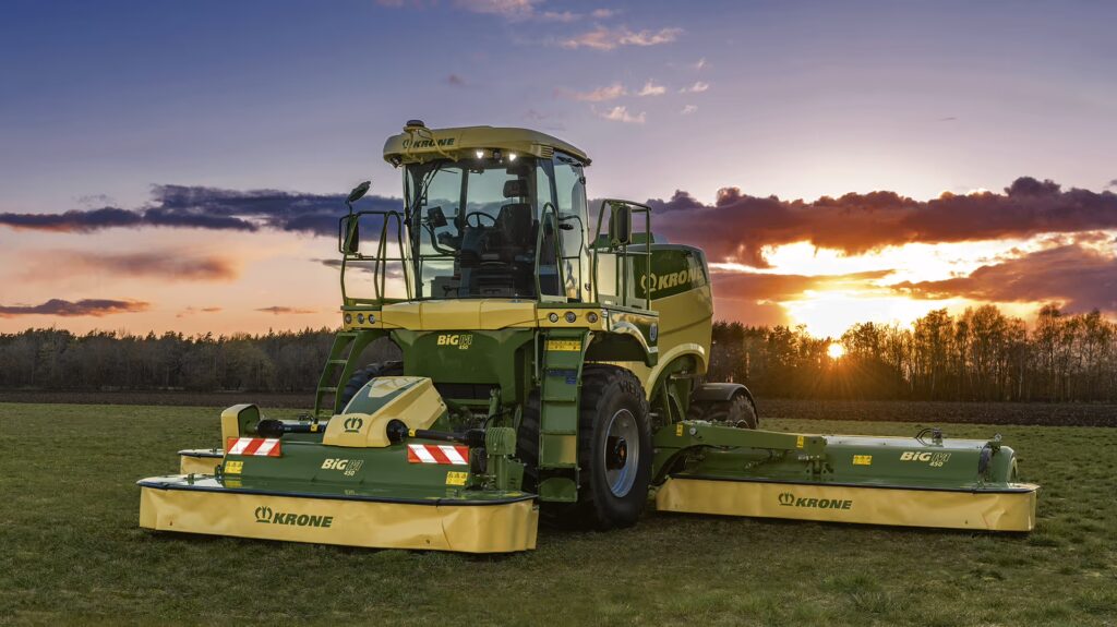 KRONE Big M 450 slåmaskin fotografert i solnedgang på slått eng. Maskinen står stille med alle tre meieskjermene utfoldet.