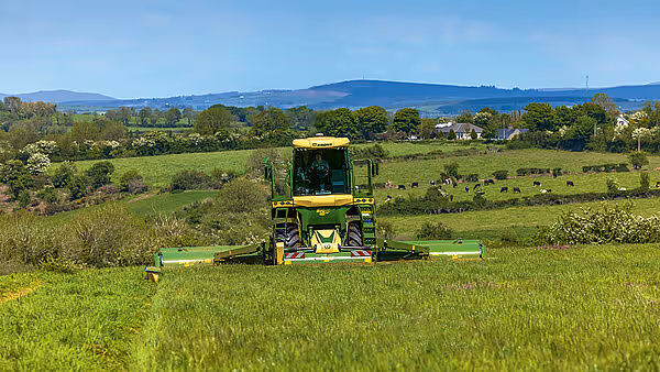 KRONE Big M 450 selvgående slåmaskin arbeider på en grønn eng med fjell i bakgrunnen.