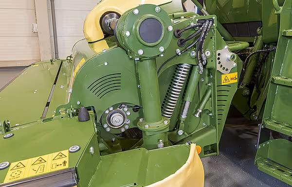 Detaljbilde av drivverket og knuseverket på KRONE Big M 450 slåttemaskin med grønne komponenter og advarselsmerker.