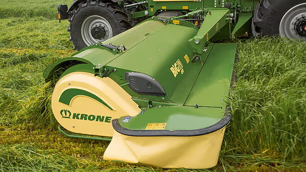 Grønn og gul KRONE slåmaskin i arbeid på gressmark, med kraftige kniver som kutter gras.