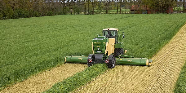 Krone Big M 450 slåmaskin i arbeid på en grønn eng, der maskinen kutter gras og etterlater seg tydelige kjørespor. Maskinen har karakteristisk grønn og gul fargekombinasjon.
