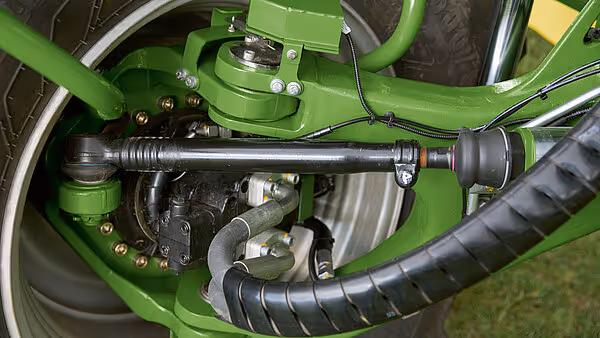 Nærbilde av hydrauliske komponenter og drivaksel på Krone Big M 450 slåmaskin. Bildet viser detaljert teknisk utstyr i grønn farge med svarte hydraulikkslanger.