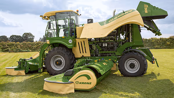 Krone Big M 450 slåmaskin fotografert fra siden på en slått eng. Maskinen har grønn og gul fargekombinasjon med løftet slåmaskinaggregat bak.