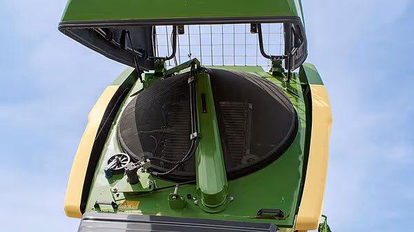 Åpen motorhjelm på Krone Big M 450 slåmaskin som viser den runde viften og kjølesystemet. Bildet er tatt ovenfra med blå himmel som bakgrunn.