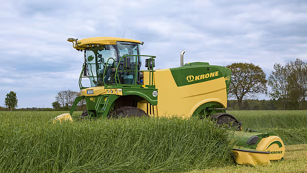 Krone Big M 450 selvgående slåmaskin arbeider i en eng med høyt gras. Maskinen har karakteristisk grønn og gul farge og er utstyrt med glasskabine.