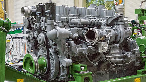 Dieselmotor i Krone Big M 450 med synlig turbolader og eksosrør. Motoren er sølvfarget og montert på grønt maskinunderlag med ulike rørledninger og komponenter.