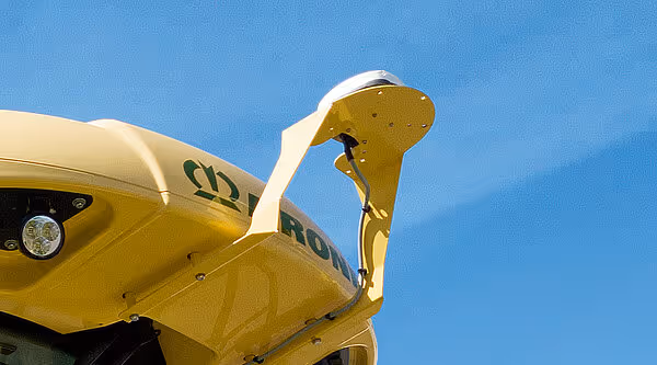 Detaljbilde av KRONE Big M slåttemaskinens gule GPS-antenne montert på toppen av maskinen mot blå himmel.