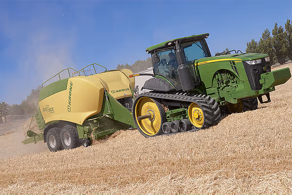 Krone BigPack Gen 5 storballpresse koblet til en grønn beltetraktor som arbeider på åker i støvete forhold.