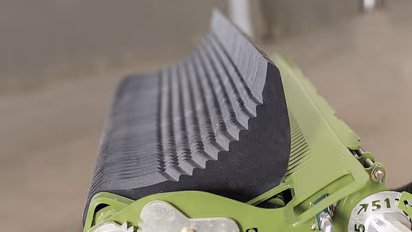 Nærbilde av oppsamlingsvalse med buede metallpigger og svart gummibelegg. Piggene er designet for effektiv høyoppsamling.