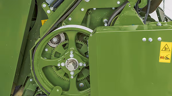 Drivverk med tannhjul og remskive på grønn KRONE pressemaskin. Mekanismen driver oppsamlings- og pressesystemet.