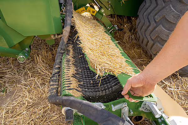 Nærbilde av strøspredemekanismen på en KRONE Big Pack Gen 5 storballpresse, med en hånd som justerer systemet for jevn strøfordeling over halmen.