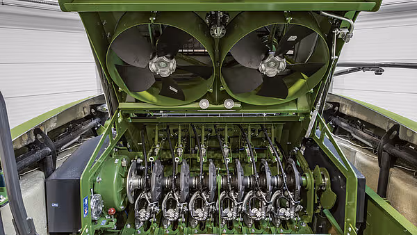 Innvendig visning av KRONE BigPack ballepresse med åpen deksel som viser komprimeringsmekanismen og vifter. De roterende elementene og hydraulikken er synlig.