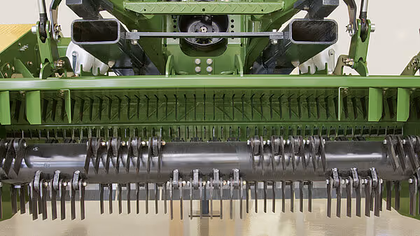 Detaljert visning av pickup-enheten til KRONE BigPack med roterende tagger og oppsamlingsmekanisme. De metalliske pinnene er arrangert i rader for effektiv oppsamling av materiale.