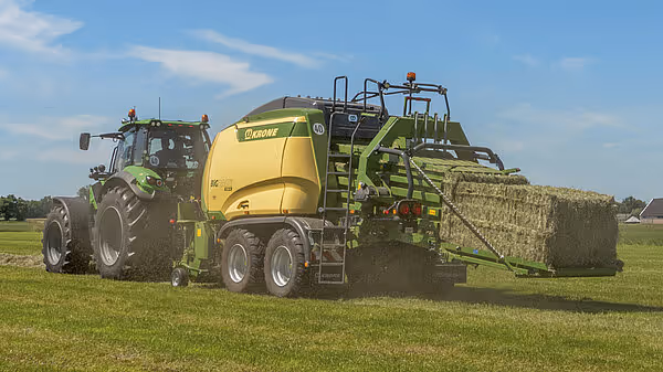 Traktor med Krone Big Pack ballepresse står på grønn eng med ferdig produsert halmballe i bakkant. Maskinen er klar til å slippe den ferdige firkantballen.