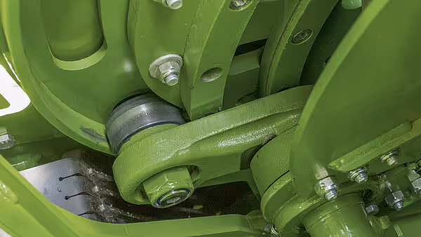 Lagring og kraftoverføring med grønne metallbraketter på KRONE storballpresse. Skruer, bolter og drivkomponenter i detaljert utførelse.