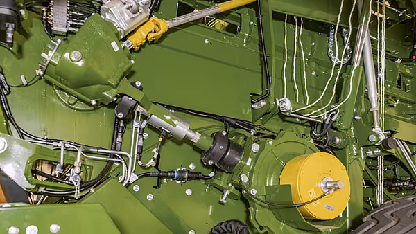 Hydrauliske sylindere og gul trommel på KRONE BigPack Gen 5 ballpresse. Komplekst system av hydraulikkslanger og styringskomponenter.