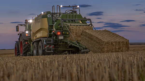 Krone Big Pack storballpresse i arbeid på kornåker ved skumring. Maskinen produserer store firkantballer av halm.