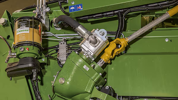 Hydrauliske komponenter og styresystem på Krone ballpresse. Gul hydraulikkmotor og grønne hydrauliksledninger er synlige.