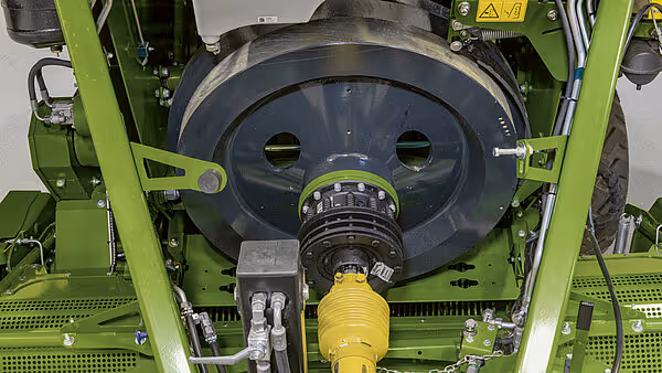 Stor svinghjul og kraftoverføring på undersiden av Krone Big Pack ballpresse. Gul PTO-aksel kobler maskinen til traktoren.