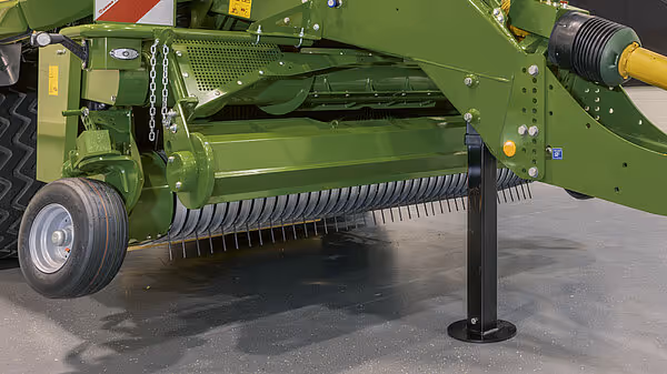 Oppsamlingsmekanisme med metallpigger på en grønn Krone rundballpress med støtteben for parkering.