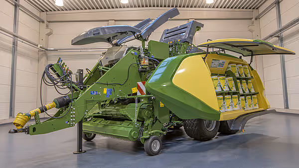 KRONE Big Pack Gen 5 ballepresse i grønn og gul farge plassert i et verksted. Maskinen har store hjul og omfattende hydrauliske systemer synlig.